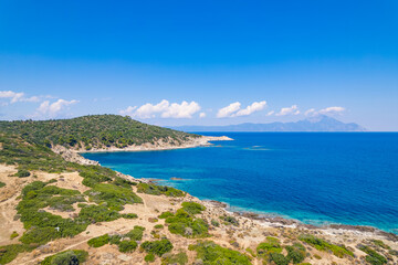 Fototapeta na wymiar Paralia Acheada, Greece. Beautiful vivid blue and turquoise seashore of a Greek island. Rocky beaches. Amazing weather with blue sky and few fluffy clouds. High quality photo