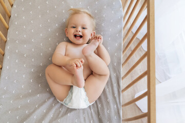 Upper view portrait of happy funny playful cute baby in diaper lying on his back playing with feet,...