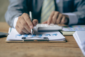 Fototapeta premium Businessman holding pen and paper pointing chart summary analysis calculating annual business report using laptop at desk in office concept accounting