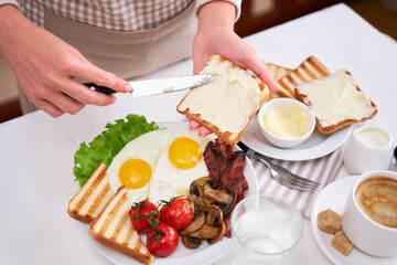 Fried eggs, bacon, tomato, toasted bread in white ceramic plate and cup of coffee
