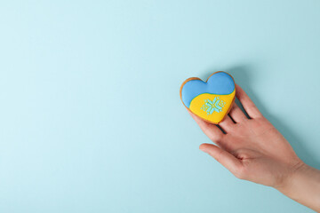 Female hand holds cookie with Ukraine flag colors on blue background