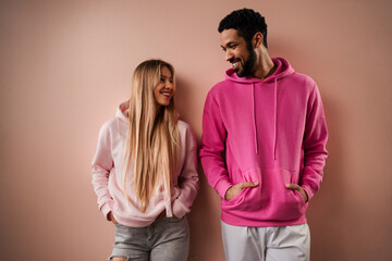 Romantic fashion studio portrait of a biracial young couple in love in hoodie posing over pink background.