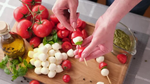 making caprese canapes sticking cherry tomatoes and mozzarella cheese balls on a skewer
