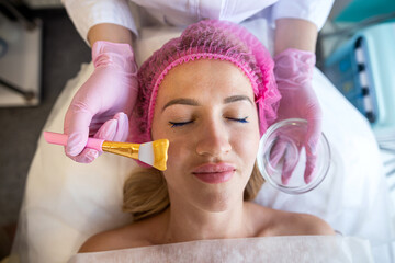 professional beautician applies a golden healing mask to a woman's face.