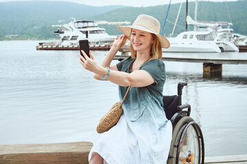 Laughing disabled woman in a wheelchair, makes a selfie on the background of sea yachts