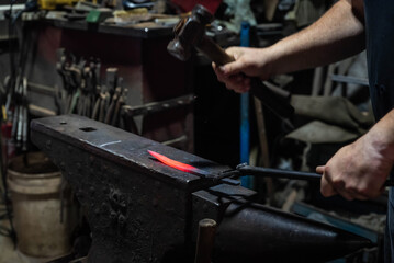 Close up view of heated metal and anvil. Blacksmith in the production process of other metal products handmade in the forge. Metalworker forging metal with a hammer into knife. Metal craft industry.