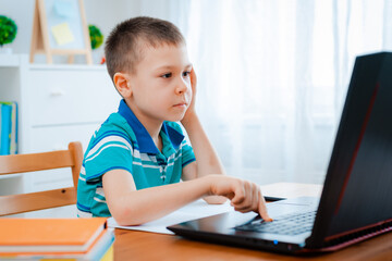 Distance learning online education. A schoolboy boy studies at home and does school homework. A home distance learning