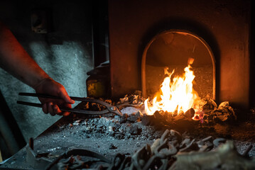 Close up view of heated metal and fire oven. Blacksmith in the production process of other metal products handmade in the forge. Metalworker forging metal into knife. Metal craft industry.