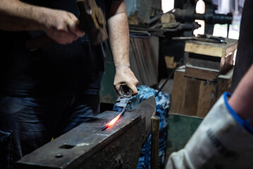 Close up view of heated metal and anvil. Blacksmith in the production process of other metal products handmade in the forge. Metalworker forging metal with a hammer into knife. Metal craft industry.