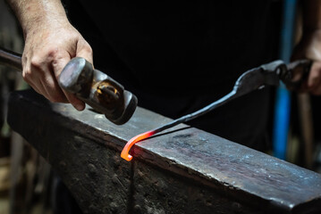 Close up view of heated metal and anvil. Blacksmith in the production process of other metal products handmade in the forge. Metalworker forging metal with a hammer into knife. Metal craft industry.