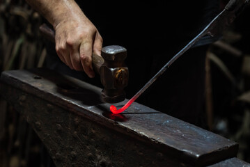 Close up view of heated metal and anvil. Blacksmith in the production process of other metal products handmade in the forge. Metalworker forging metal with a hammer into knife. Metal craft industry.