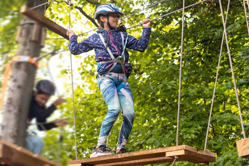 Little girl preschooler wearing full climbing harness having fun time in the rope park using carabiner and other safety equipment. Summer camp activity for kids. Adventure park in the forest