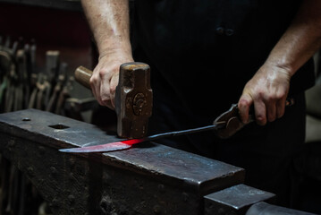 Close up view of heated metal and anvil. Blacksmith in the production process of other metal products handmade in the forge. Metalworker forging metal with a hammer into knife. Metal craft industry.