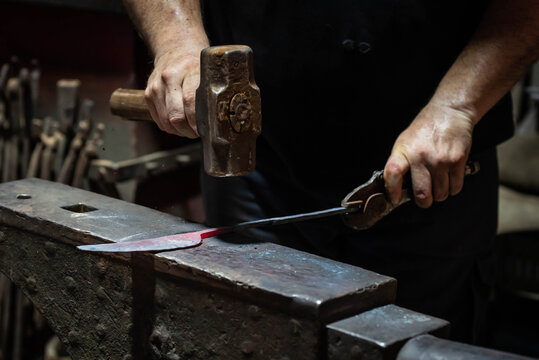 Close up view of heated metal and anvil. Blacksmith in the production process of other metal products handmade in the forge. Metalworker forging metal with a hammer into knife. Metal craft industry.