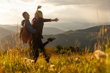 Naklejka na ściany i meble Happy traveler young couple resting in the mountains at sunset in spring or summer season.