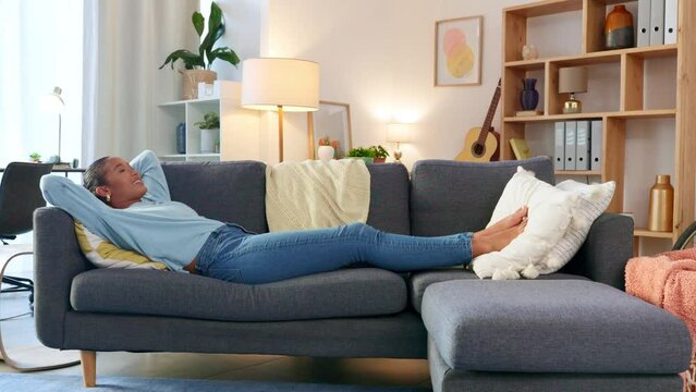 Happy and relaxed woman lying with hands behind her head on home living room sofa as new property homeowner. Relieved, accomplished and carefree real estate investor in a purchased house