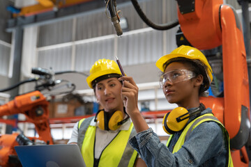 Women Engineer wearing helmet and hi visible vest using laptop computer working in factory welding robotic automation happy smiling with quality control and programming pass 
