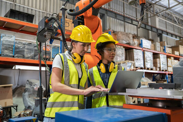 Women Engineer wearing helmet and hi visible vest using laptop computer working in factory welding robotic automation happy smiling with quality control and programming pass 
