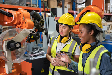 Women Engineer wearing helmet and hi visible vest using laptop computer working in factory welding robotic automation happy smiling with quality control and programming pass 
