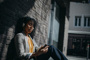 Young biracial woman wearing headphones and enjoying listening to music outdoors in street.