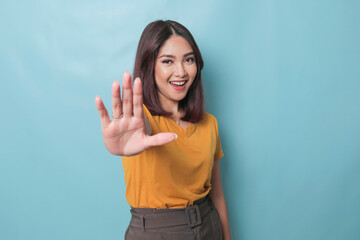 Young Asian woman wearing casual t-shirt over blue isolated background doing stop sign with palm of...