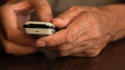 A button phone in the wrinkled hands of an elderly person