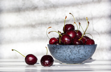 Ripe red cherries in a bowl and next to it on wooden table.