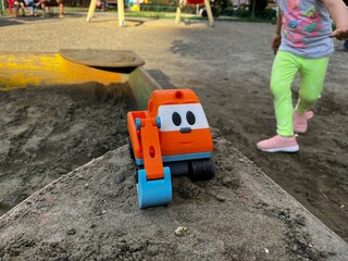 Fototapeta na wymiar A child slinking to their toy excavator left on the edge of a sandbox on a playground