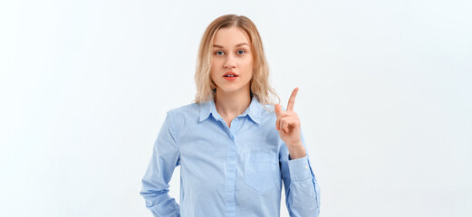 You better not. Serious blonde girl is frowning, pointing fingers up, stands in blue shirt. Indoor studio shot on white background