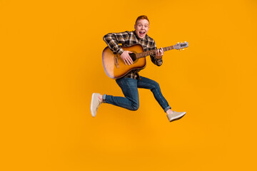 Full body photo of young guy jump up play guitar performance acoustic isolated over yellow color...