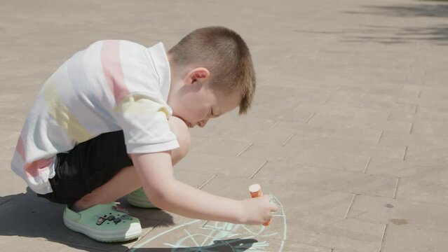 4K. A boy draws with colored crayons on the asphalt