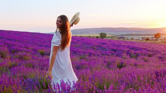 Young woman in white dress walking through a lavender field on sunset