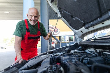 Senior mechanic checking the oil level in the car engine.