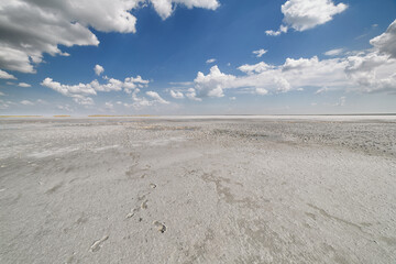Fototapeta na wymiar Dried salt lake layer of salt, blue sky and clouds