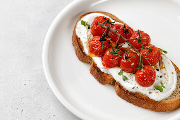 Toast, snack, bruschetta with ricotta cheese, cream cheese and baked tomatoes cherry on white plate. Healthy vegetarian sandwiches with whole grain bread.