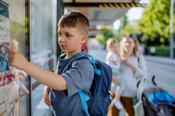 Young mother with little kids waiting on bus stop in city.