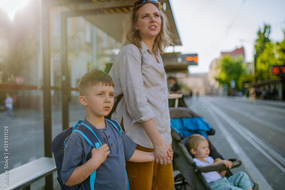 Wall mural young mother with little kids waiting on bus stop in city.