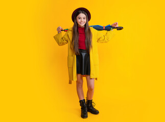 Happy teenager portrait. Child teenager girl with rainbow umbrella in autumn weather isolated on yellow background. Autumn kids clothes. Smiling girl in autumn coat.