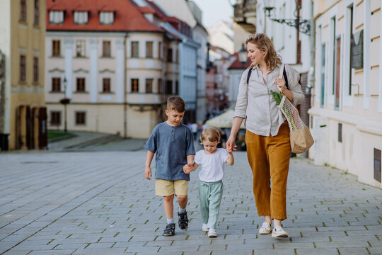 Young mother with zero waste shopping bag holding hands with her children and walking in city street street