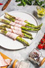 Fresh green asparagus wrapped in bacon on grey concrete table