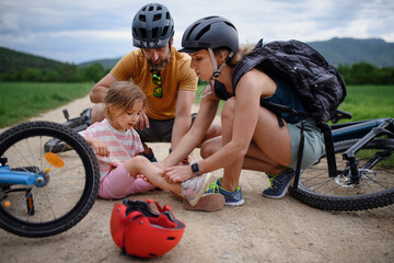 Mother and father helping their little daughter after falling off bicycle outdoors