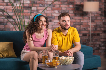 At home in front of tv good looking couple watching a football match together they getting happy when their team are winning they hugging each other and drinking some beer