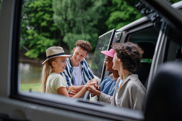 Multiracial young friends travelling together by car, standing by car and smiling - summer...