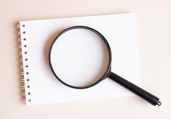 The magnifying glass lies on the notebook on a white page.