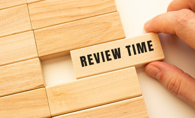 Hand holds a wooden cube with the text REVIEW TIME.