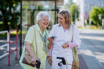 Portrait of caregiver with senior woman on walk in park with shopping bag, laughing and talking.