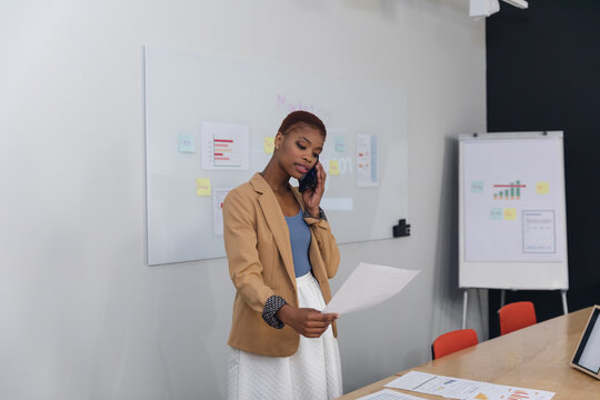 African american young businesswoman talking on smart phone and analyzing document in office