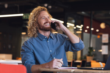 Happy young caucasian businessman looking away while talking on smart phone in creative office
