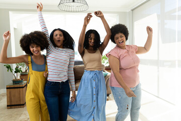 Carefree biracial female friends dancing and having fun in living room during weekend, copy space
