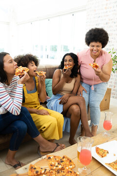 Millennial biracial friends enjoying pizza and drinks while spending leisure time together at home